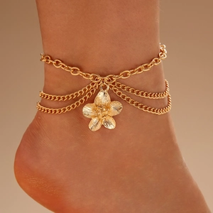 Detail of a layered gold anklet featuring a textured flower pendant and chunky chain