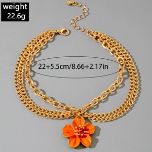 Detail showing triple-layer golden chain anklet with orange flower pendant and lobster clasp