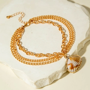 Detail of gold layered anklet with shell pendant on a textured white stone tray
