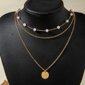Détail d'un collier doré à trois couches avec perles d'imitation et pendentif disque rond