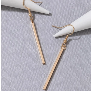Detailed close-up of gold geometric bar drop earrings on textured grey background