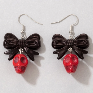 Détail de boucles d'oreilles nœud noir brillant avec crânes rouges sur fond gris
