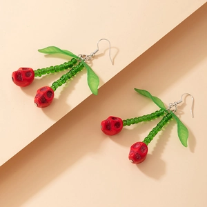 Détail de boucles d'oreilles cerise tête de mort avec perles rouges et feuilles vertes