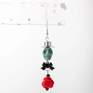 Détail de boucle d'oreille gothique avec crâne turquoise, nœud noir et rose rouge