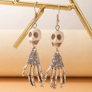 Détail de boucles d'oreilles tête de mort et main squelette sur un support doré chic