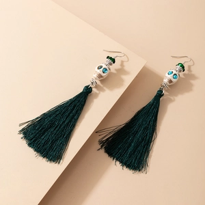 Détail de boucles d'oreilles à longs pompons verts avec crâne et accents bleus