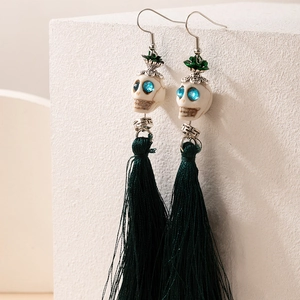 Détail macro de boucles d'oreilles tête de mort avec glands verts et pierres bleues