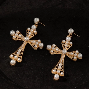 Détail de boucles d'oreilles croix dorées avec perles sur velours noir