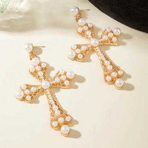 Vue rapprochée de boucles d'oreilles croix dorées avec perles sur fond beige