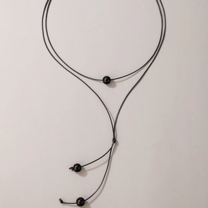 Minimalist black braided cord Y-shaped necklace with polished spherical beads on grey background