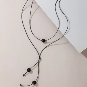 Minimalist Y-shaped woven necklace with black beads on a sleek geometric background