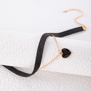 Detail of black suede choker with gold chains and a heart pendant on white pedestal