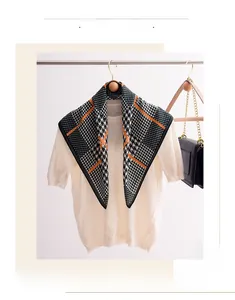 Close-up of houndstooth scarf with orange stripes styled on a beige knitted sweater