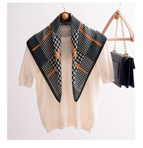 Detail of black houndstooth square scarf with orange trim on a wooden hanger