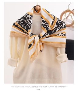Detail of silk scarf with leopard print and gold chain pattern on beige sweater