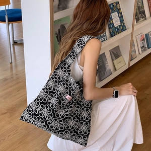 Détail d'un sac cabas en tricot noir avec broderies marguerites et étiquette rose