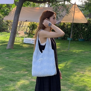 Detail of light blue floral embroidery on canvas hobo bag against green grass backdrop