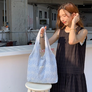 Detail view of light blue daisy embroidery on a soft fashion tote bag with brand label