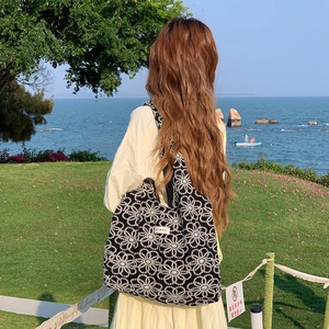 Rear view of a black canvas tote bag with white floral embroidery on a scenic beach background