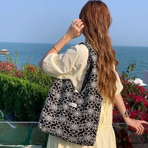 Detail of black tote bag with white daisy embroidery on a summer beach background