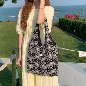 Detailed shot of a black canvas tote with daisy embroidery in a seaside park setting