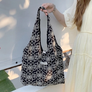 Close-up of intricate white floral embroidery on a black canvas tote bag with a woven tag