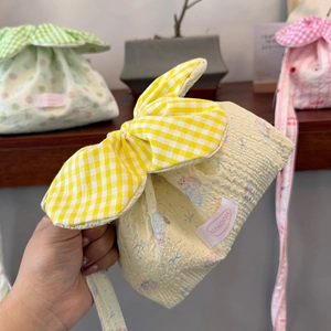 Detail of yellow seersucker drawstring bag with a large checkered bow and woven brand label