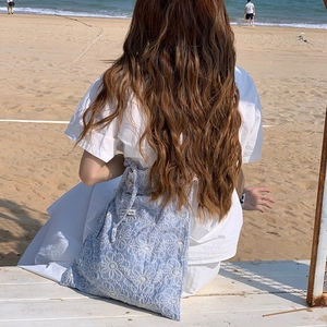 Close-up of light blue floral embroidery on a large crossbody bag at a sunny beach