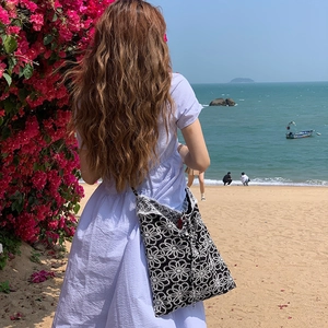 Outdoor shot of a woven lace tote bag with white daisy embroidery and sea background