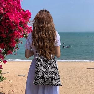 Close-up of black tote bag with white daisy lace crochet details on a sunny beach
