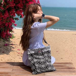Black lace tote bag with white daisy embroidery and bow detail on beach background