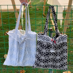 Détail de sacs cabas en dentelle brodée de fleurs bleues et noires avec petits nœuds