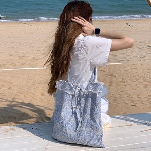 Détail du sac cabas en dentelle bleu clair avec broderie florale et volants à la plage