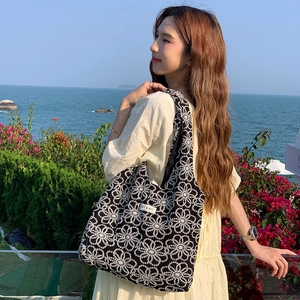 Black tote bag with white daisy embroidery and korean label on a scenic seaside background