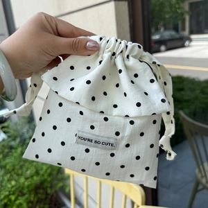 Close-up of white drawstring bag with black polka dots and You are so cute slogan label