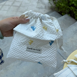 Detail of white drawstring bag with bird embroidery and 'YOU'RE SO CUTE' label