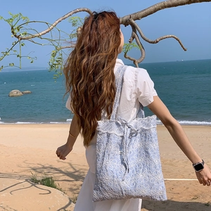 Sac cabas bleu clair avec broderie florale et dentelle sur fond de plage ensoleillée