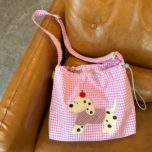 Détail du sac bandoulière vichy rose avec écusson dalmatien sur un canapé en cuir