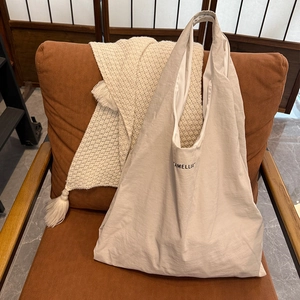 Détail du logo Camellia sur un cabas beige en nylon posé sur un fauteuil douillet