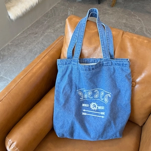 Detail of blue denim tote bag with white paisley print on a brown leather sofa
