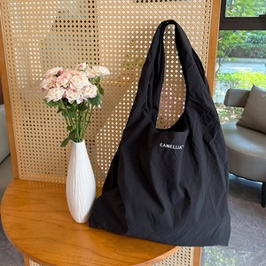Gros plan du sac fourre-tout noir en nylon avec texte Camellia blanc sur bois