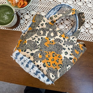 Detail of orange leopard print tote with denim trim and fringe on lace tablecloth