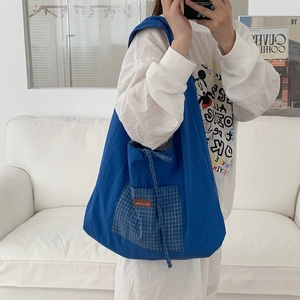 Détail du sac cabas en toile bleue avec poche avant à carreaux et écusson en cuir marron