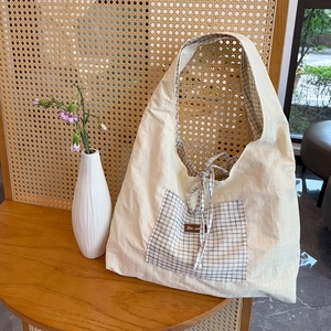 Détail du sac cabas en toile avec poche à carreaux bleus et étiquette en cuir marron