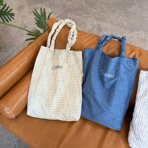 Detail of plaid fabric tote bag featuring embroidered logo and ruched handle texture