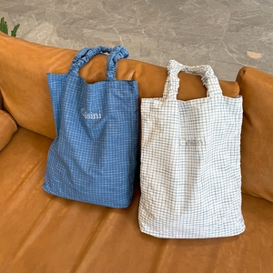 Detail of checkered tote bags with ruffled handles and Cisini embroidery on leather sofa