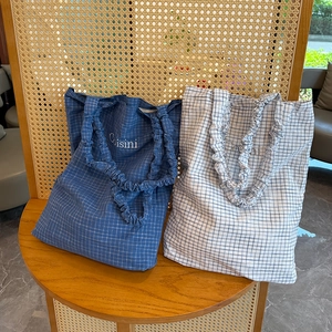 Detail of Korean-style plaid tote bags with ruffled handles and Coisini print on a chair