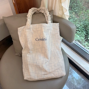 Detail of light blue checkered tote bag with scrunched handle and embroidered Coisini text