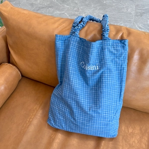 Close-up of blue checkered tote bag featuring Coisini embroidery and ruffled handle detail