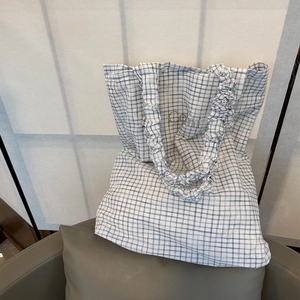Blue and white checkered tote bag with ruched handles and embroidered logo on a sofa